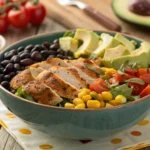 A colorful bowl of Southwest Chicken Salad with grilled chicken, black beans, corn, avocado, cherry tomatoes, and fresh greens.